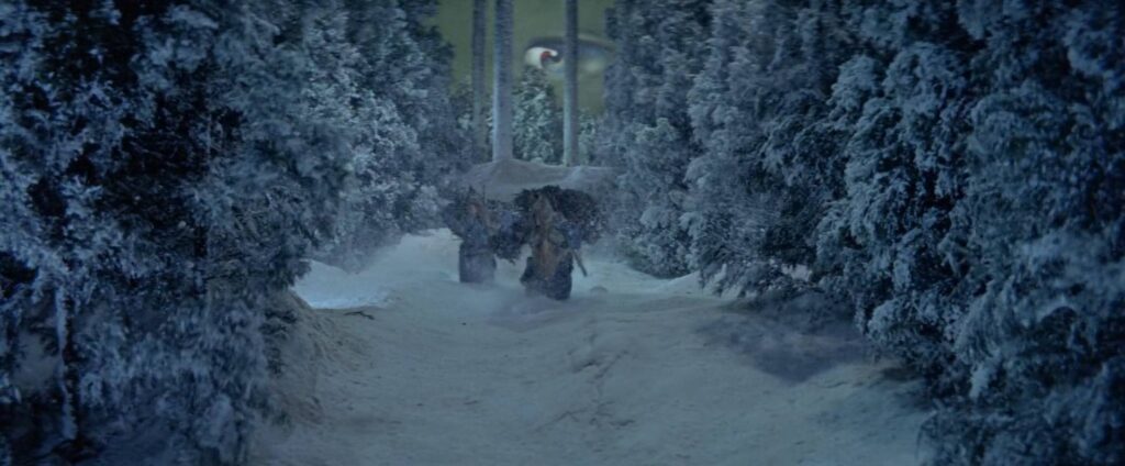 Two woodcutters trudge through a snowstorm in a forest with heavy, painted snow-laden trees in The Woman of the Snow segment of Kwaidan.